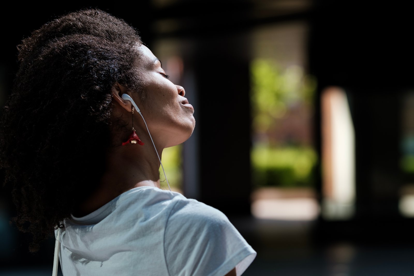 Back view of black woman using headphones outdoors in a hot summer day. She is listening to music and relaxing.
